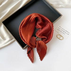 Detailed view of caramel pleated silk scarf artfully arranged on a sleek black tray
