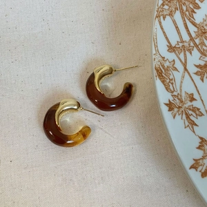 Macro detail of C-shaped amber resin earrings with polished golden metallic finish