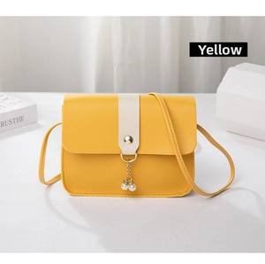 Detail view of yellow crossbody bag featuring cream stripe and white pearl pendant charm