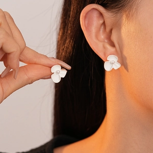 Detailed close-up of matte white flower stud earrings with a pearl center on a model