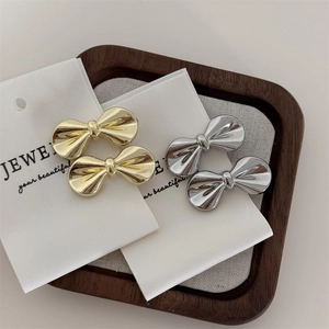 Set of four stylish gold and silver metal bow hair clips on a minimalist white card display