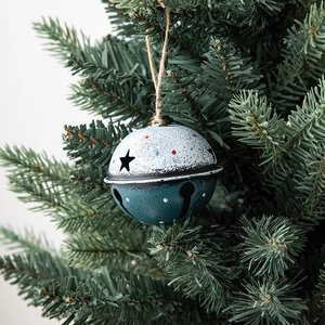 Vintage metal Christmas bell ornament with rustic star cutouts hanging on a green tree