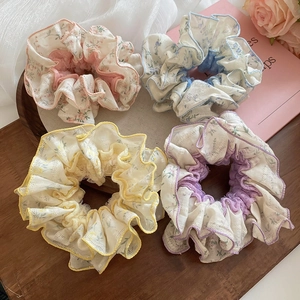 Detail view of four floral lace scrunchies in pink, blue, yellow, and purple on a wood tray