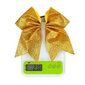 Close-up of gold glitter bow hair tie with rhinestones on a scale weighing 23.6 grams