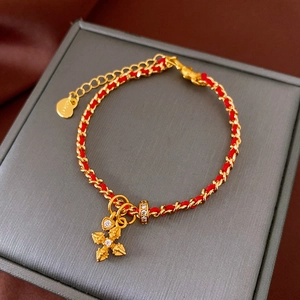 Detail of red braided string bracelet with gold cross charm and heart tag on velvet