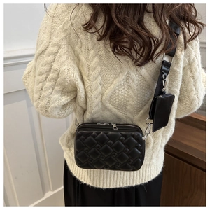 Detail of black quilted crossbody bag with adjustable strap and small coin pouch