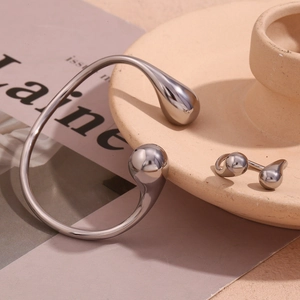 Detail of silver teardrop cuff bracelet and ring set on minimalist beige pottery