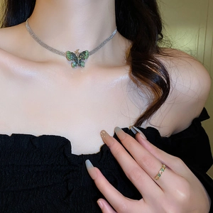 Close-up of a silver mesh necklace featuring a vibrant green crystal butterfly pendant