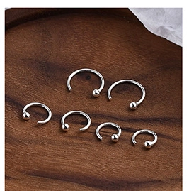 Macro shot of six assorted silver horseshoe piercings on a rustic wood background