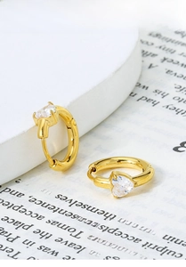 Detail of gold heart zirconia earrings with titanium steel hoops on an elegant background