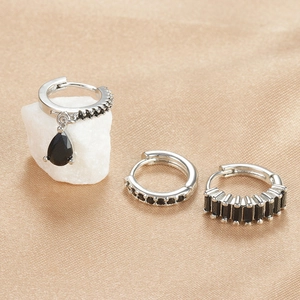Detailed close-up of three geometric silver earrings with black zircon stones on silk