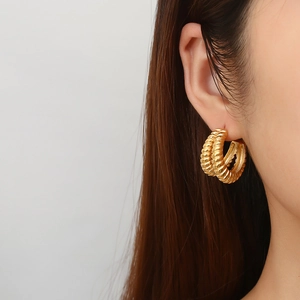 Detail of vintage golden C-shape geometric earrings with textured spiral design on model