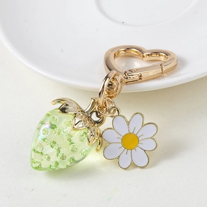 Detail of green strawberry pendant and white daisy charm with heart-shaped gold hook