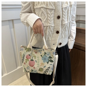 Detail view of floral embroidery on beige canvas shoulder bag with adjustable strap