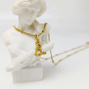 Collier doré avec pendentif lettre B et cœur sur buste de sculpture blanc
