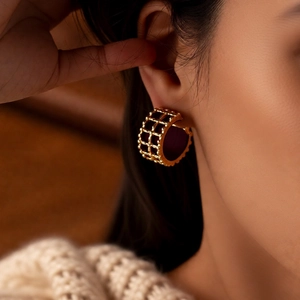 Close-up of golden geometric hollow hoop earrings worn with a beige knitted sweater