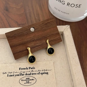 French minimalist gold earrings with round black agate on warm wooden display base