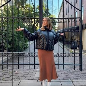 Short black glossy puffer jacket paired with a brown pleated knit skirt and white boots