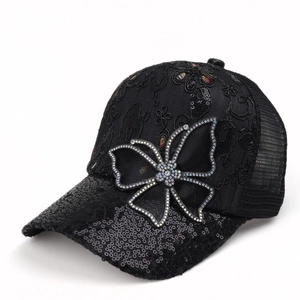 Detail of a black baseball cap with lace fabric, sequins, and a rhinestone bow ornament