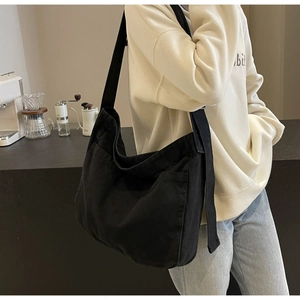 Detail of a large black canvas tote bag showing the side pocket and wide woven shoulder strap