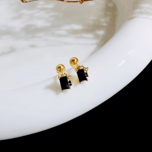 Macro shot of gold stud earrings featuring black stones and delicate bow details
