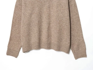 Detail view of ribbed hem and cuffs on soft tan knit sweater with textured fabric