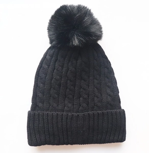 Close-up of the black cable knit texture and faux fur pom-pom on the warm winter hat