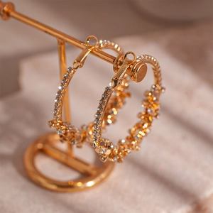 Close-up of golden geometric hoop earrings with sparkling white crystals on a gold stand