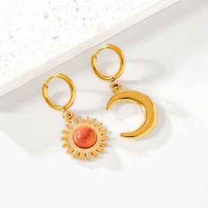 Detail of asymmetrical gold sun and moon earrings with orange gemstones on stone
