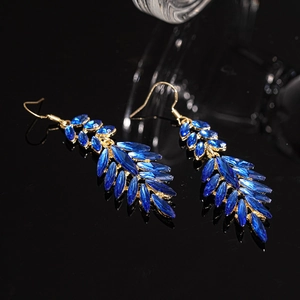Detailed view of luxury gold leaf earrings with deep blue crystals on black mirror surface