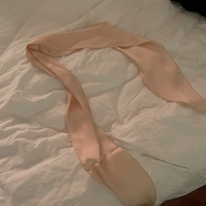 Detail of soft apricot silk ribbon scarf draped elegantly on white cotton bedding fabric