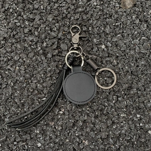 Macro shot of a black braided leather fringe keychain with metal hardware on asphalt