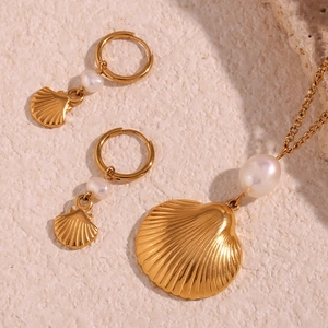 Macro shot of 18K gold plated shell necklace and pearl earrings on sand background