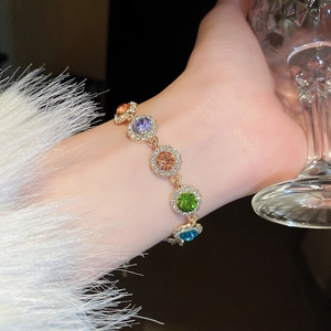 Close-up of a luxury gold bracelet featuring colorful gemstones and pave zircon on model