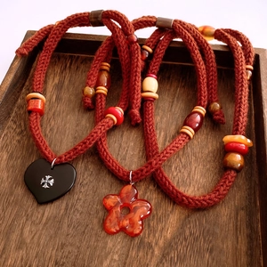 Detail of plush heart pendant necklace with woven rope and floral charms on wood