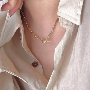 Detailed close-up of a gold OT toggle clasp necklace worn over a white shirt