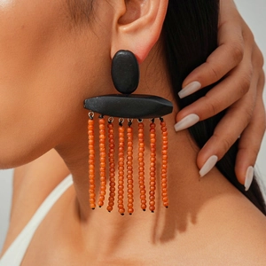 Close-up of ethnic style earrings with black geometric top and orange beaded tassels