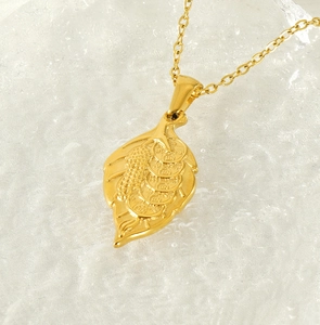 Detail of golden leaf pendant with lucky fish and coin relief on ice texture background