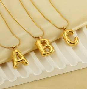 Detail of three 18K gold balloon style alphabet pendants A B C on sleek snake chains