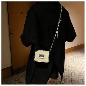 Detail of beige quilted square bag with metal chain strap worn on shoulder by model