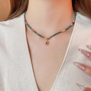 Gros plan d'un collier de perles avec pendentif soleil doré et pierre rouge sertie