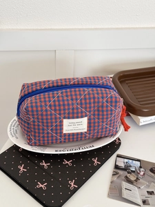 Detail of quilted checkered toiletry bag with red tassel zipper and blue grid pattern