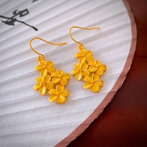 Macro detail of matte gold flower drop earrings with a vintage floral design