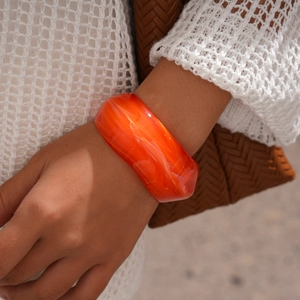 Close-up of a wide orange acrylic bangle with white marble texture on a model wrist