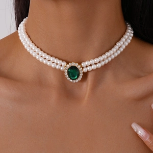 Detail of double-layer faux pearl necklace with oval green emerald and zircon accents