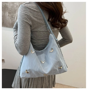Detail of light blue shoulder bag with silver butterfly charms on wrinkled glossy fabric