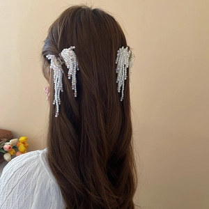 Detailed view of artificial pearl tassel hair clips on model in a half-up hairstyle