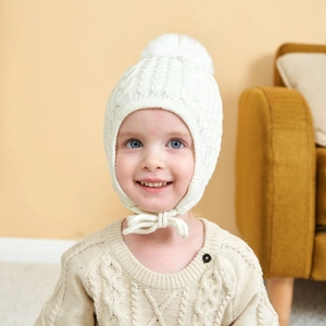 Toddler knitted winter hat in cream white featuring cozy earflaps and a white pompom