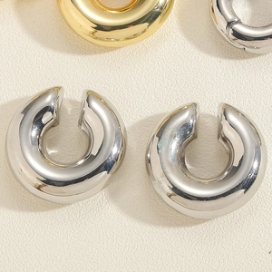 Macro view of C-shaped ear cuffs in polished gold and silver finishes on a textured background