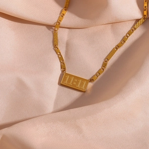 Macro detail of 11:11 rectangular gold pendant on silk fabric with pig nose chain